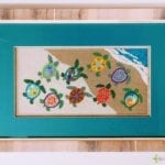 framed turtle needle point with turquoise mat and heavy wood grain frame.